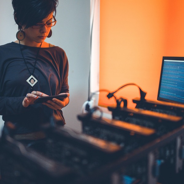 Person checking a phone next to a home CPU mining rig with multiple units and a monitor