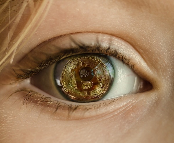 Close-up of a human eye with a bitcoin-style coin reflected in the iris, symbolizing blockchain visibility and surveillance